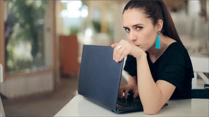 Обеспокоенная женщина прикрывает ноутбук для уединения.